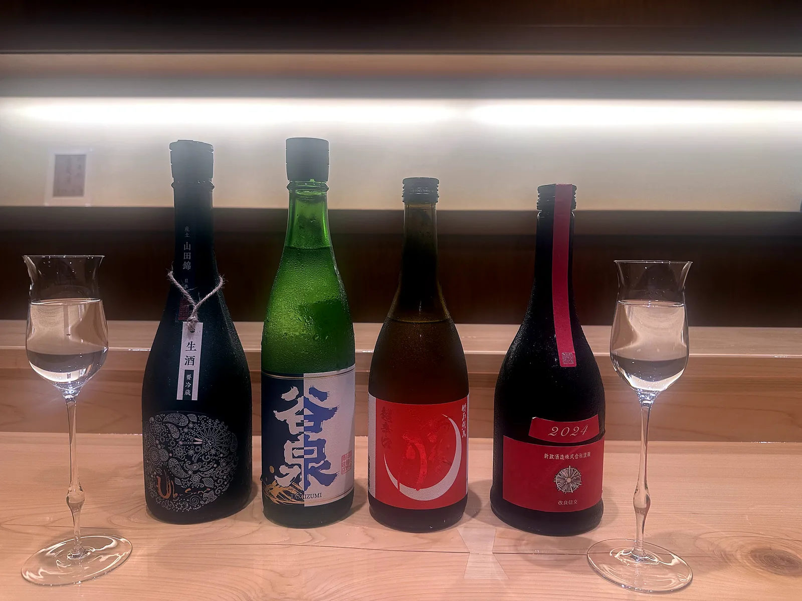 カウンターに並ぶ日本酒四本と盃